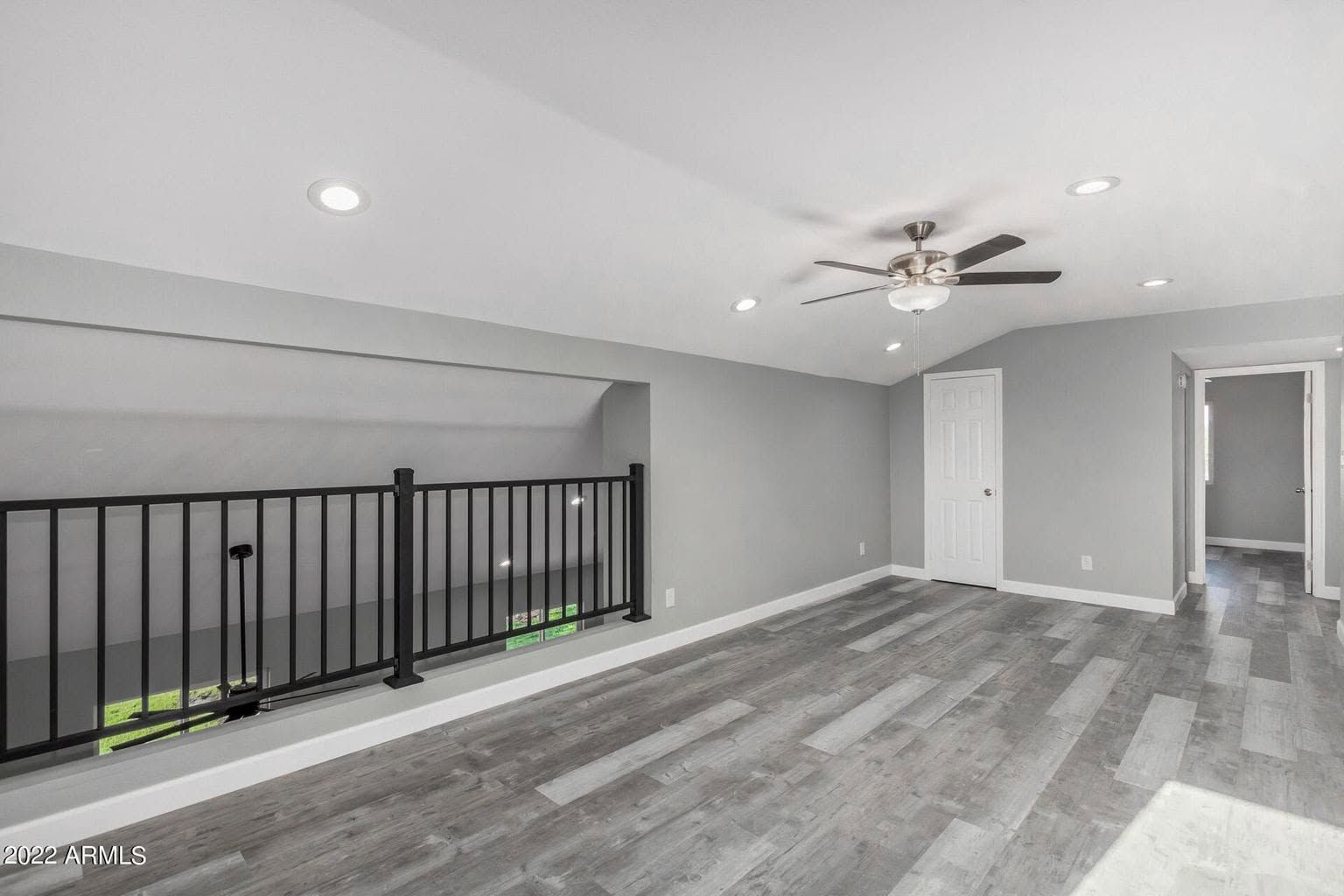 Bright modern loft with gray walls, wood floors, black railing, ceiling fan, and doorway at right
