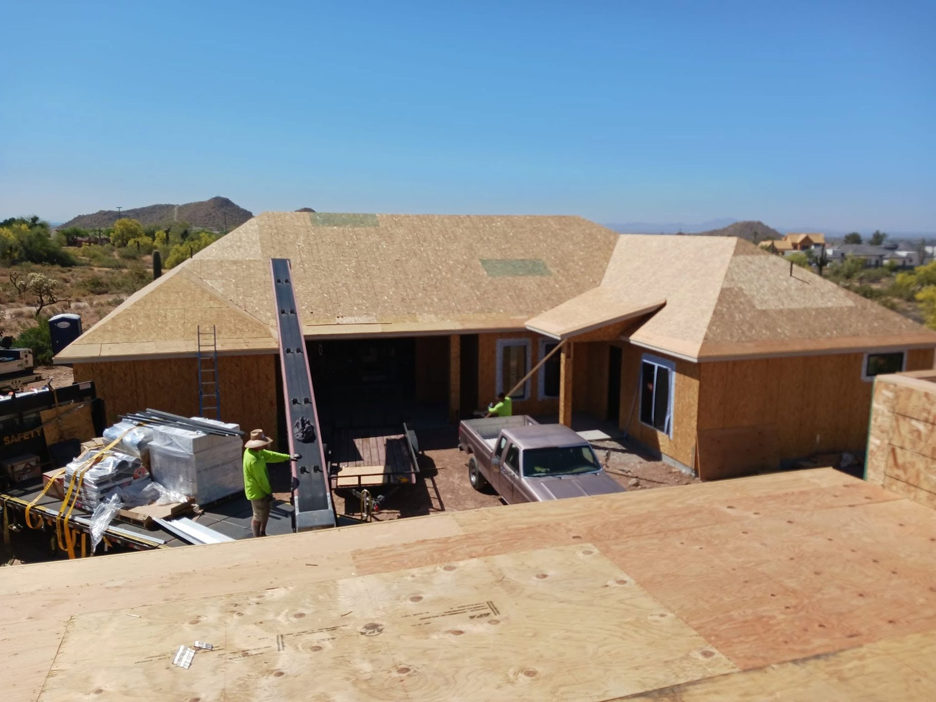 Construction site with workers roofing a large house under clear blue sky