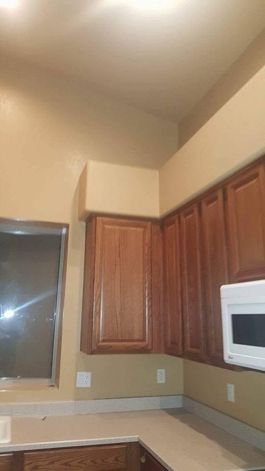 Empty beige kitchen with wooden cabinets, white microwave, and a vaulted ceiling.