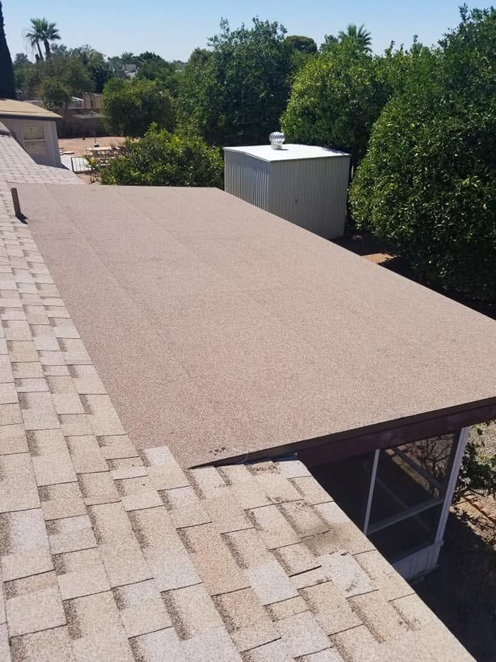 Tan gravel-covered roof above a brick patio beside green trees and a white rooftop unit