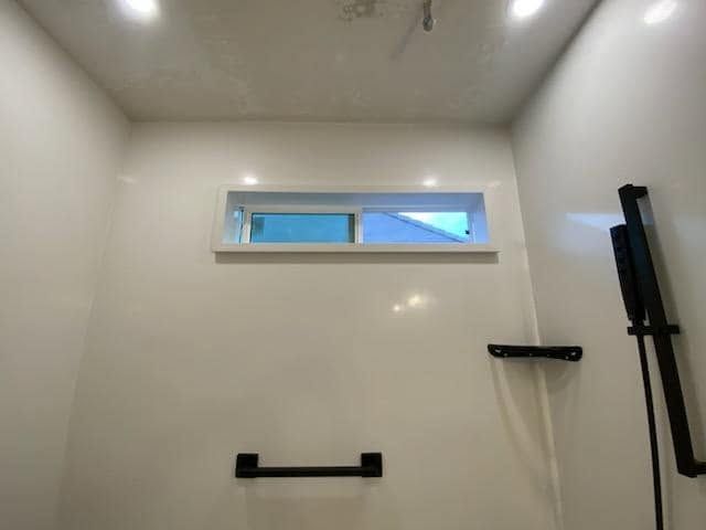 Empty white shower stall with glass shelf, grab bars, and black shower fixtures