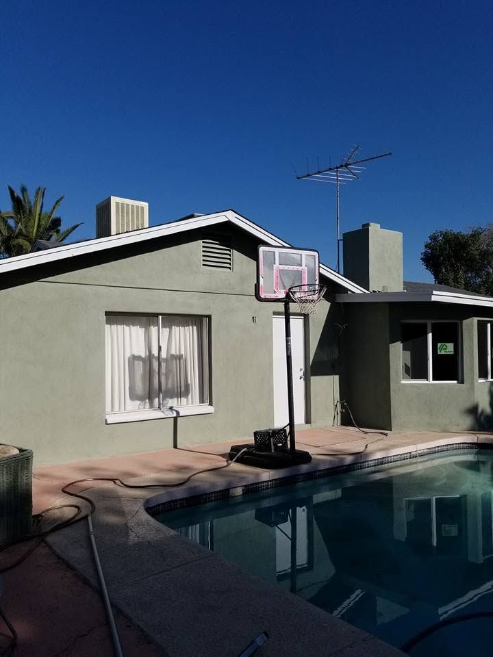 Backyard pool with a portable basketball hoop beside a gray house under a clear blue sky
