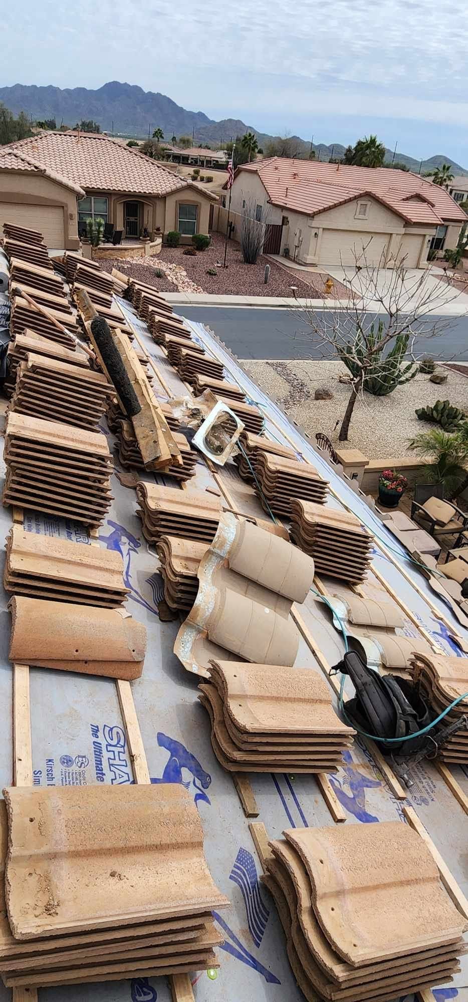 Roofing materials stacked on a sloped roof, with houses and mountains in the background.