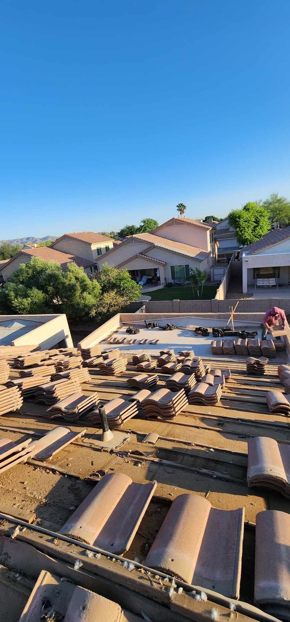 Roof tiles stacked on a rooftop with suburban houses and blue sky in the background