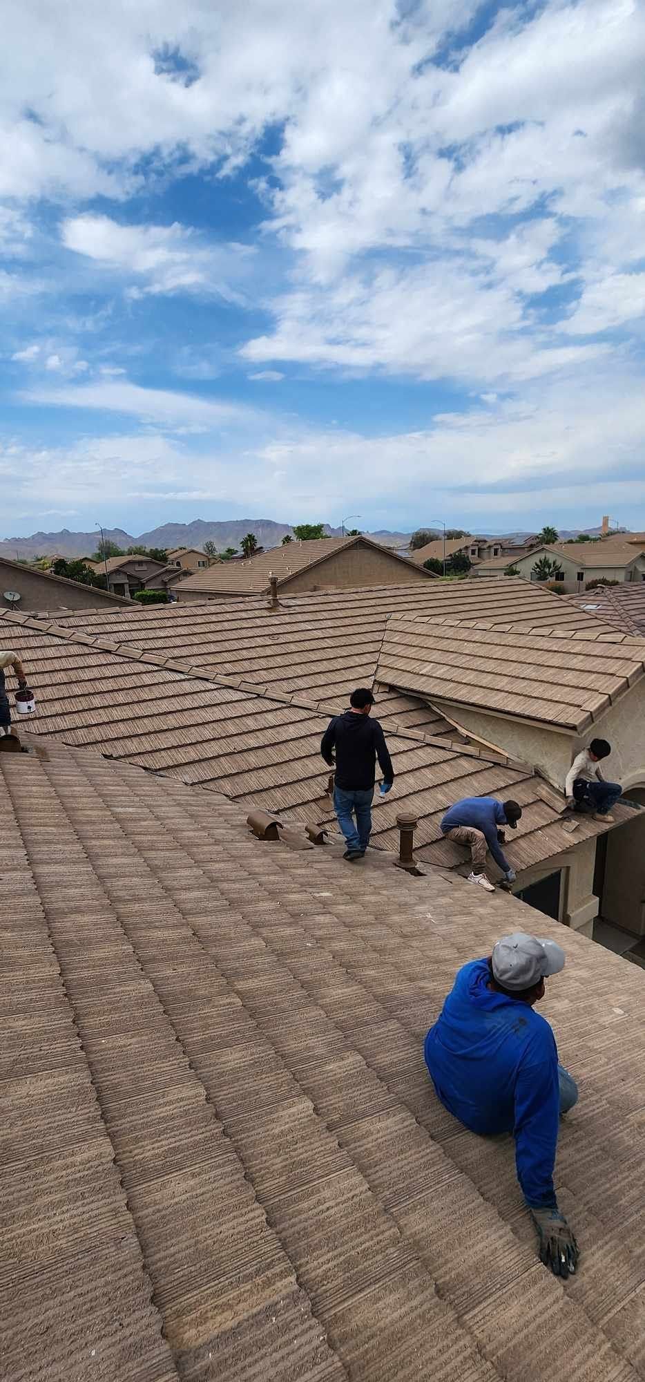 Workers repairing a shingled roof under a partly cloudy sky