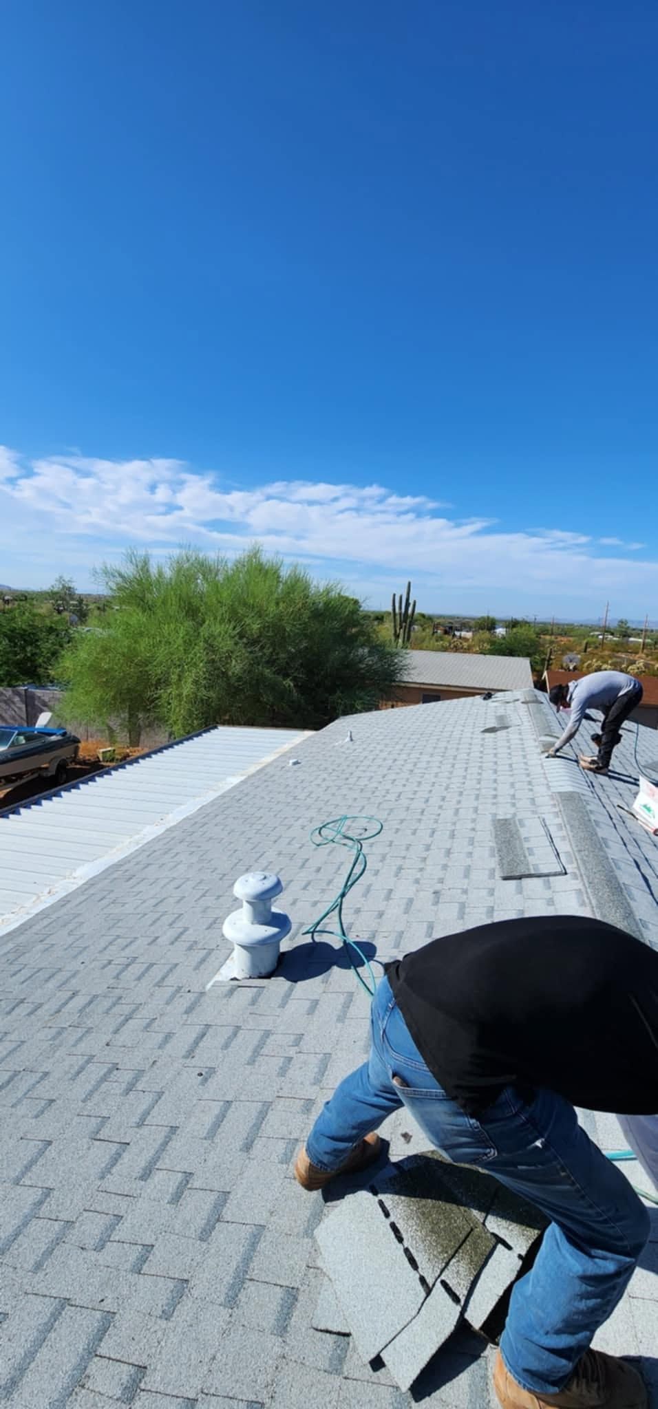 Workers installing roofing on a sloped rooftop under a clear blue sky