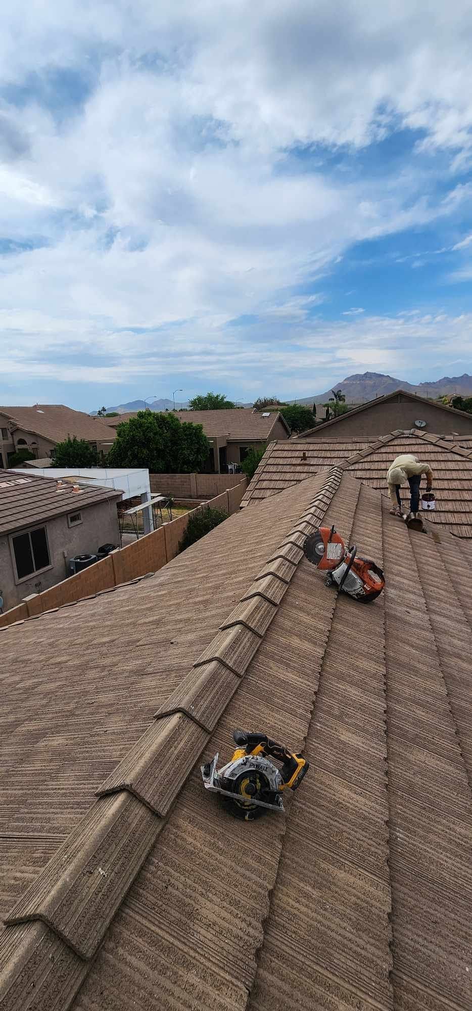 Workers on a tiled rooftop under a blue sky, repairing shingles in a suburban neighborhood.