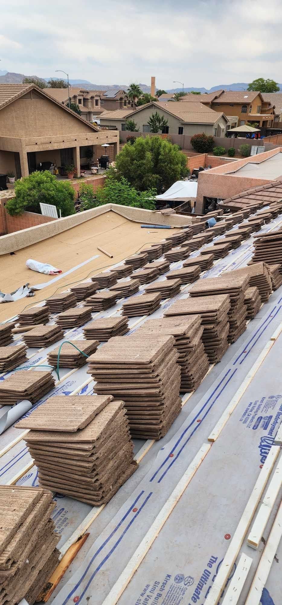 Stacks of roof tiles on a rooftop with houses and trees in the background