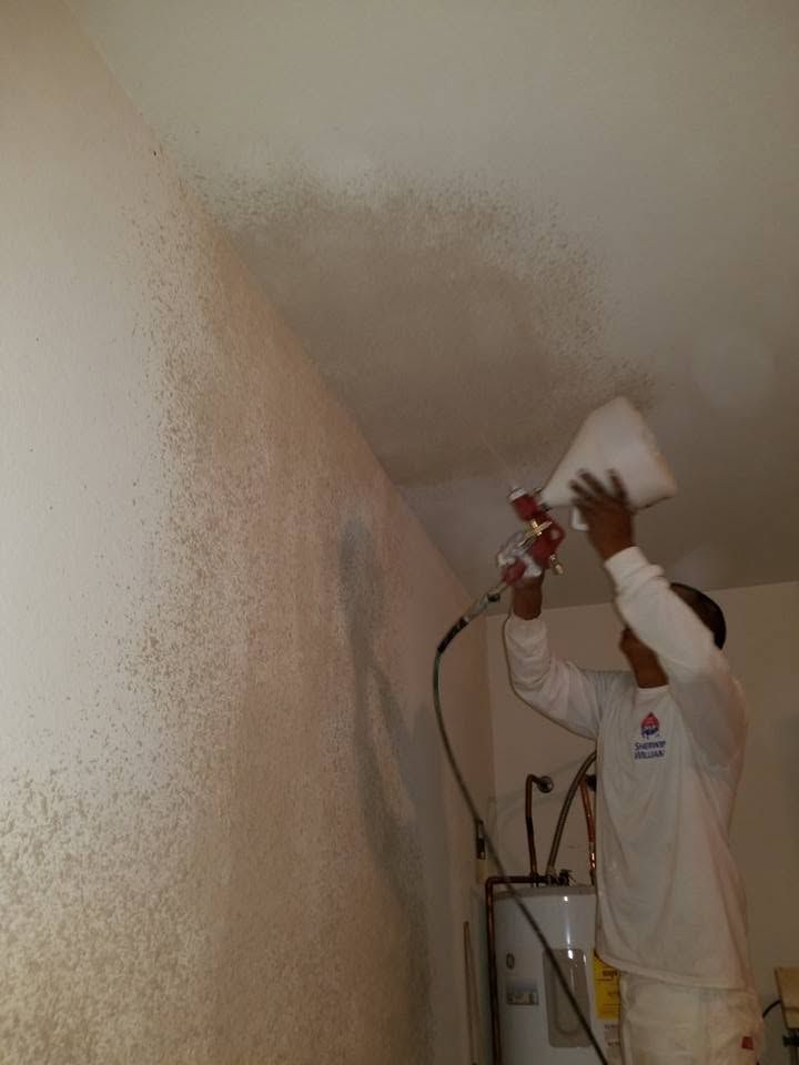 Worker spraying white paint on a ceiling and wall in a room