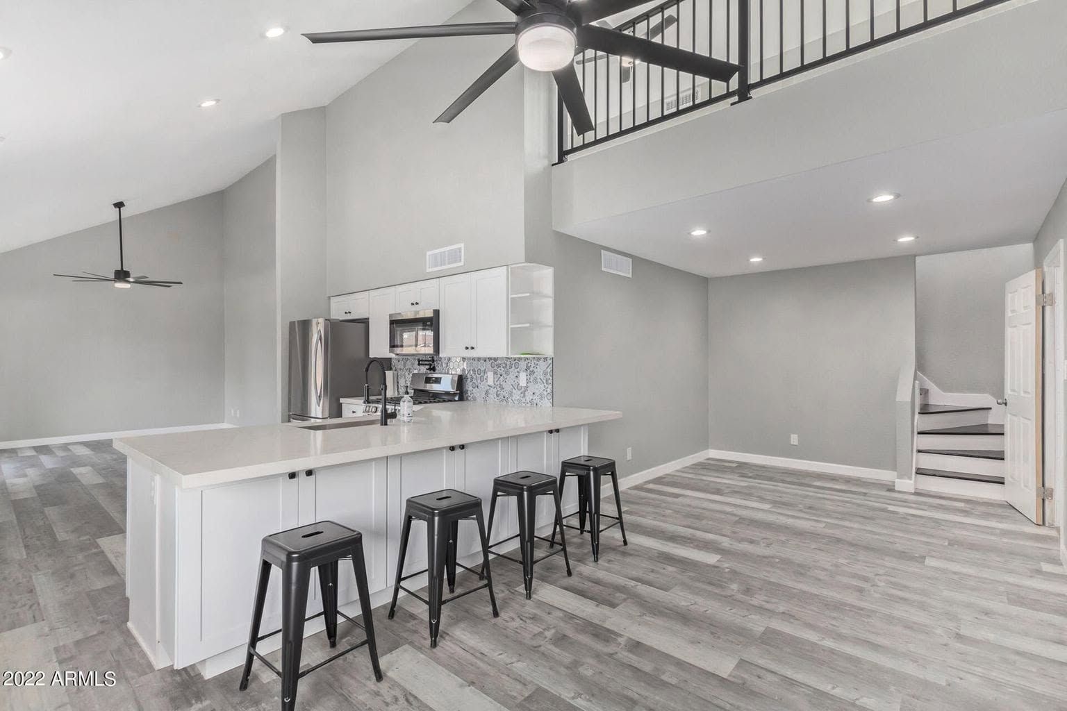 Bright modern kitchen with island bar stools, gray floors, staircase, and open loft ceiling