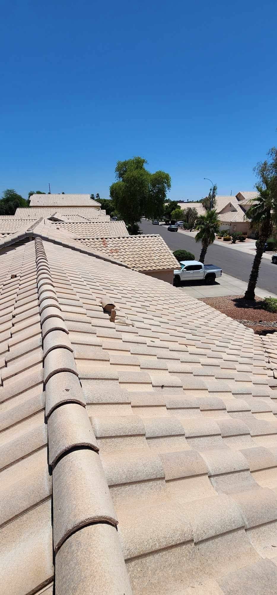 Rooftop view of beige tiled homes and palm trees along a sunny suburban street, with a white car parked below