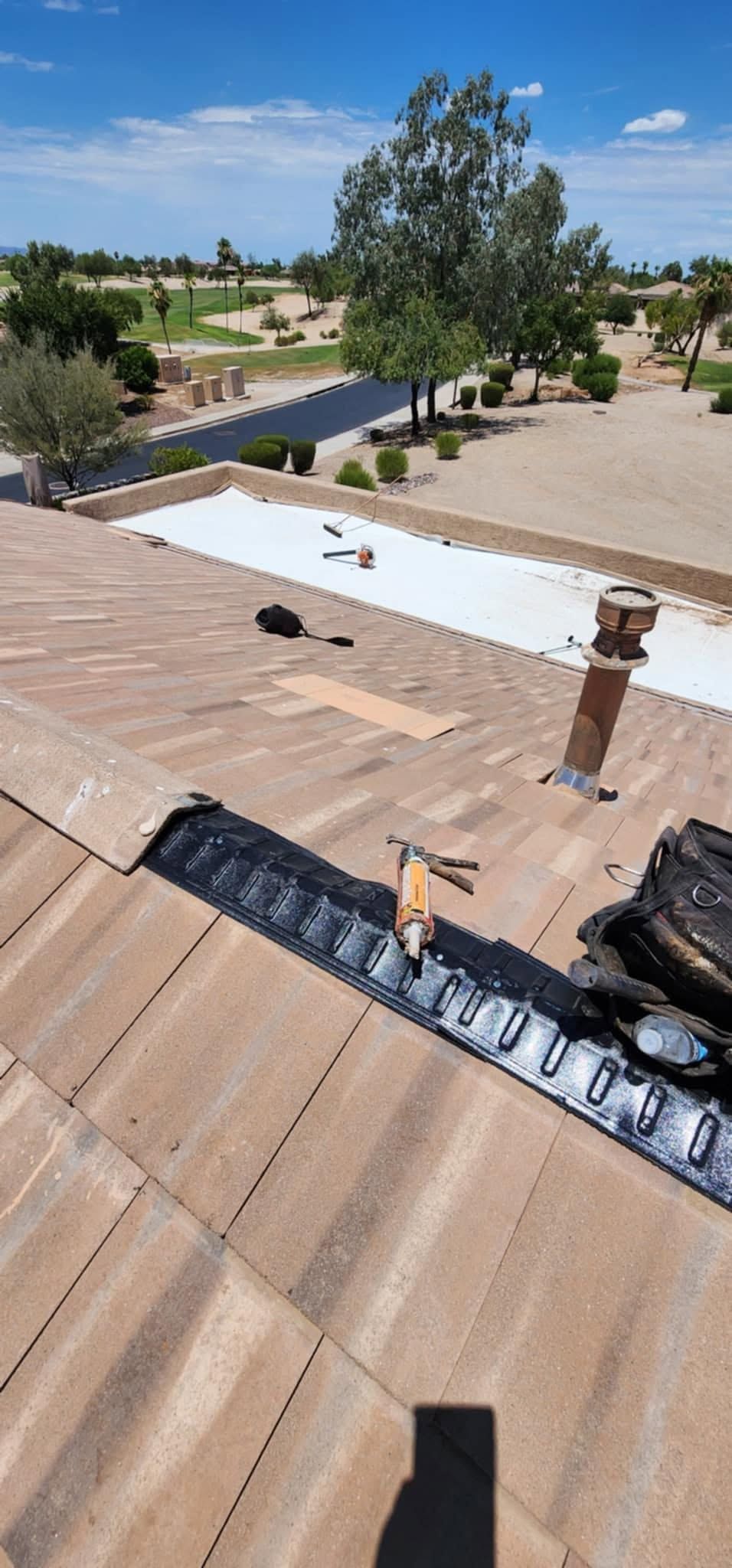 Rooftop with damaged shingles and exposed white underlayment overlooking a dry neighborhood and trees