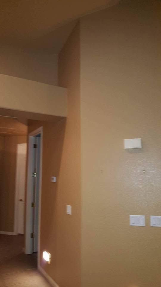 Tan hallway with beige walls, doorway, light switch, and a small floor light near the baseboard.
