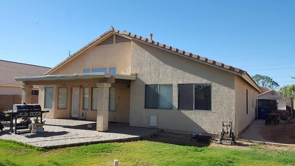Single-story beige stucco house with a covered front porch and small lawn under a clear blue sky