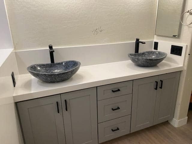 Double vanity with two black stone sinks and gray cabinets in a bathroom