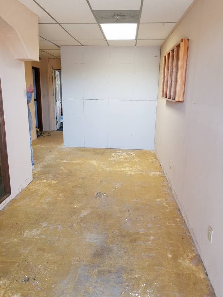 Empty narrow hallway with unfinished flooring, white wall panels, and fluorescent ceiling lights