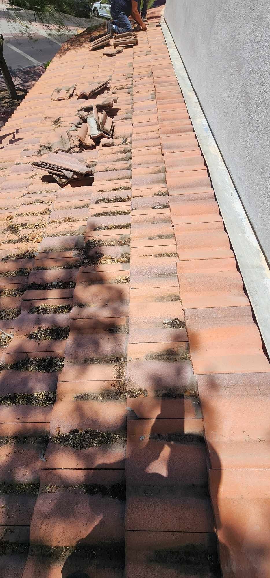 Sidewalk covered with broken bricks and debris beside a white wall in strong sunlight