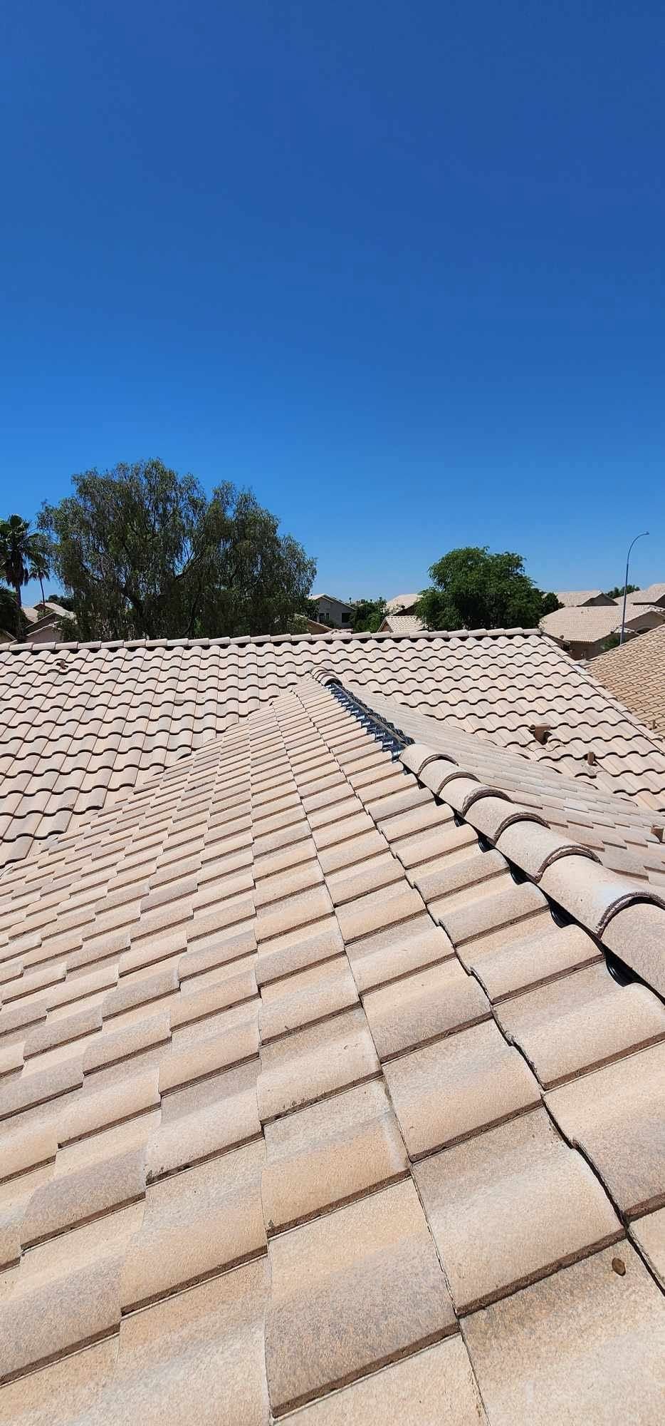Sunlit tan tile roof with a small blue repair patch under a clear blue sky