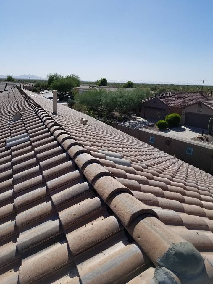 Rooftop view of tan clay tiles overlooking a suburban neighborhood and distant fields under a clear blue sky