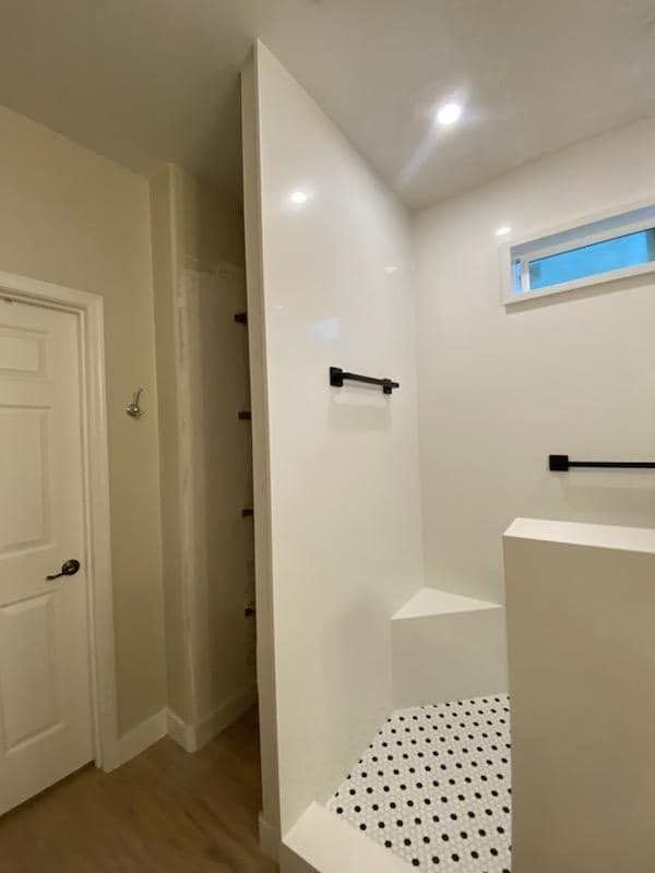 Bright bathroom with white walls, black fixtures, and a tiled shower bench next to a hallway door.