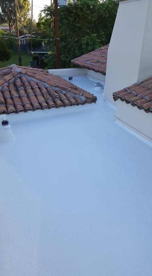White rooftop terrace with terracotta-tiled roof sections and a central chimney, overlooking greenery