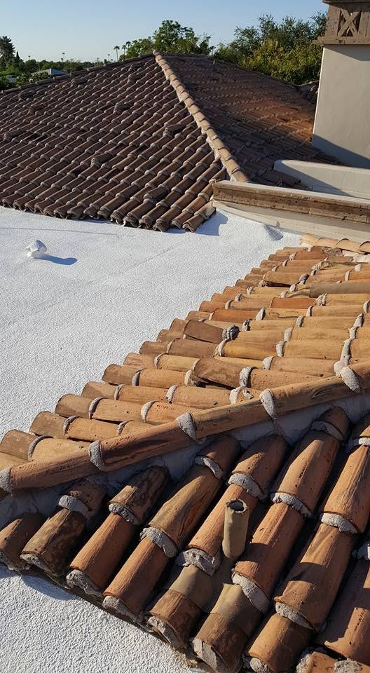 Close-up of terracotta roof tiles and a white flat roof under bright sunlight, with trees in the background