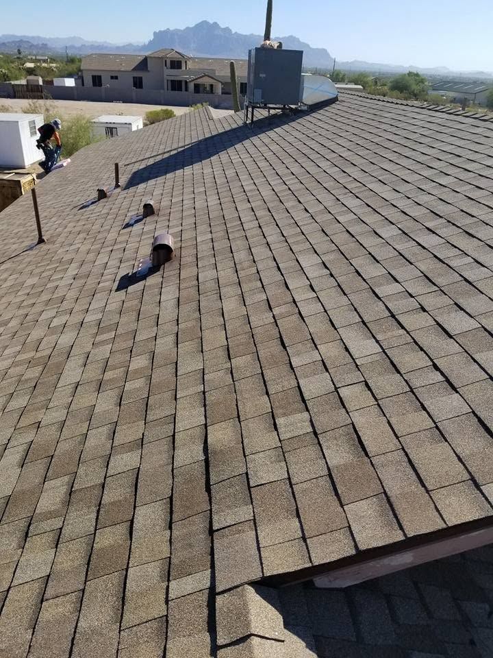 Roofer on a shingled roof under clear sky, with mountain view in the distance.