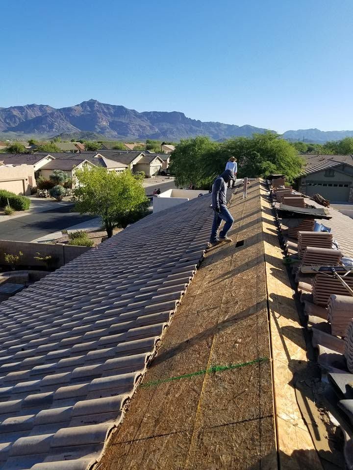 Worker on a roof under repair, standing on exposed roofing with mountains and homes in the background.