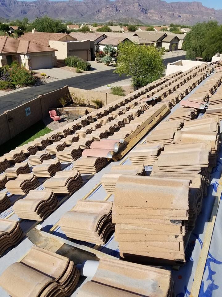 Stacks of beige roof tiles drying outdoors on racks in a suburban neighborhood with mountains in the background