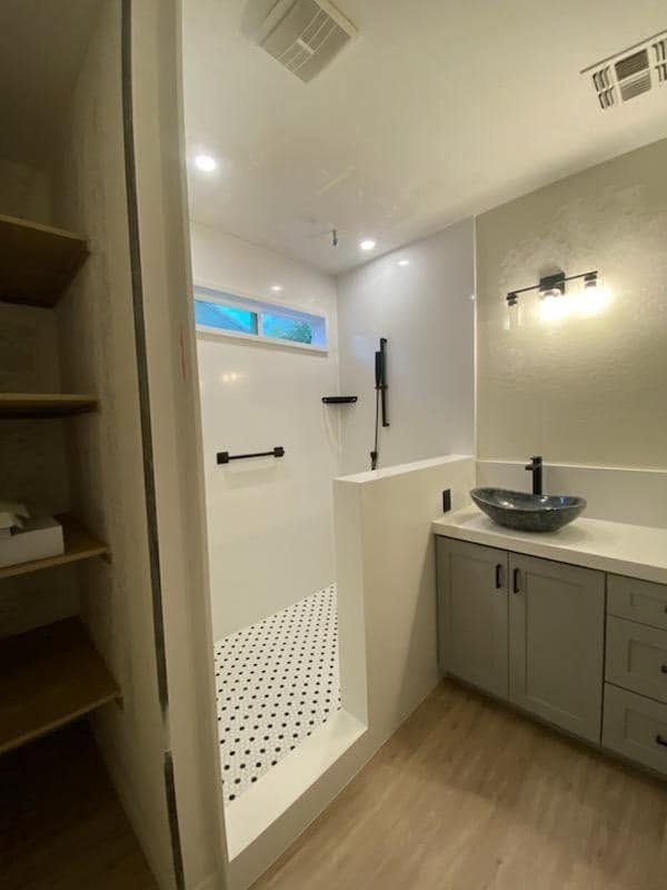 Modern bathroom with walk-in shower, gray vanity, and wood floor, viewed from the doorway