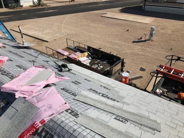 Roof under construction with pink underlayment, tools, and a black debris chute