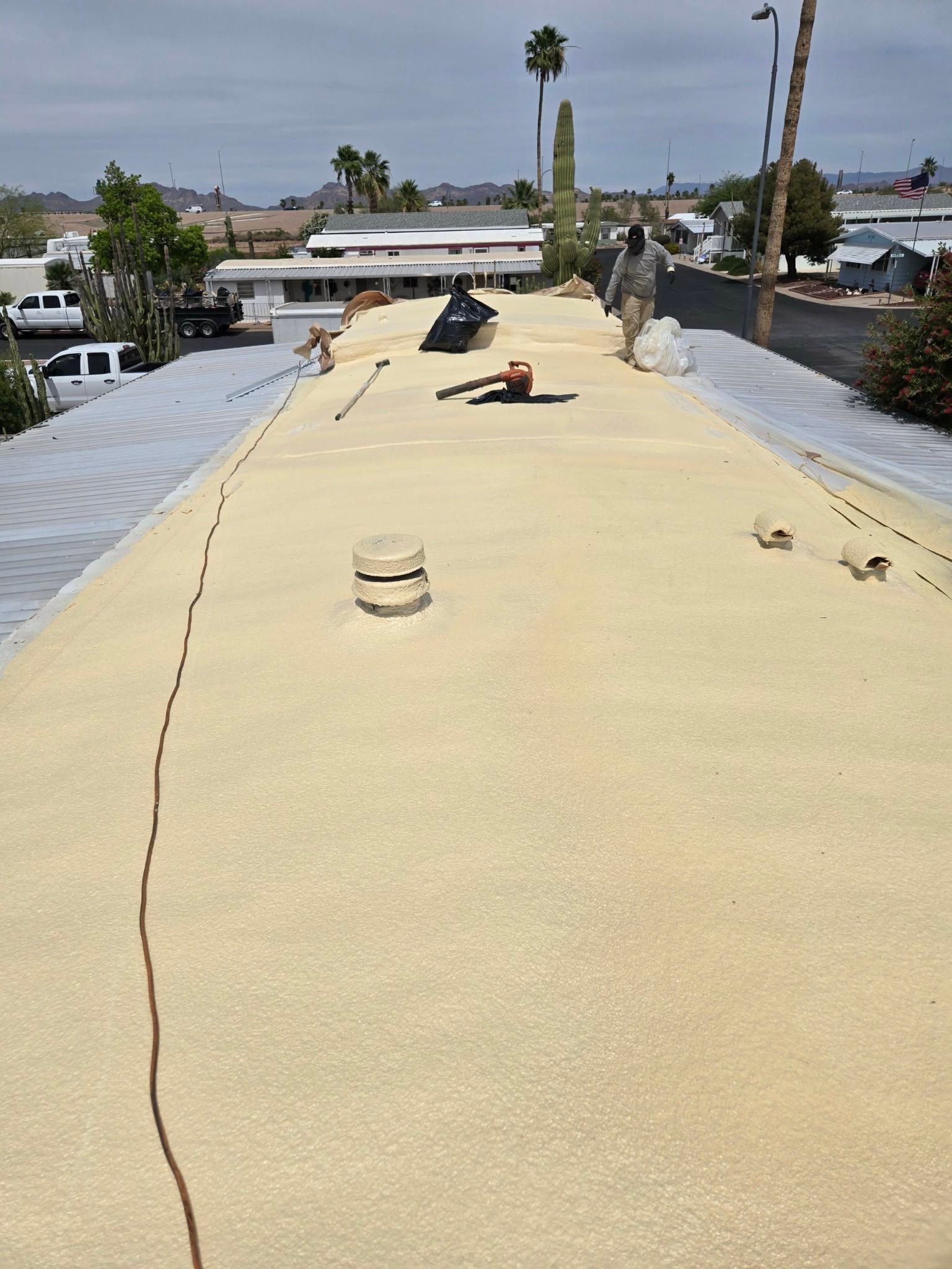 Rooftop with beige coating, scattered tools, and a worker near the center under a bright sky