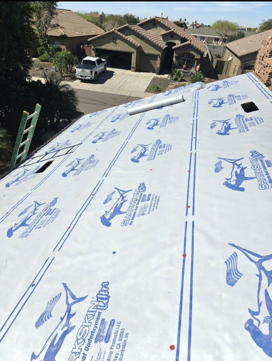 White roofing underlayment on a sloped roof, overlooking houses and a parked truck in a sunny neighborhood.