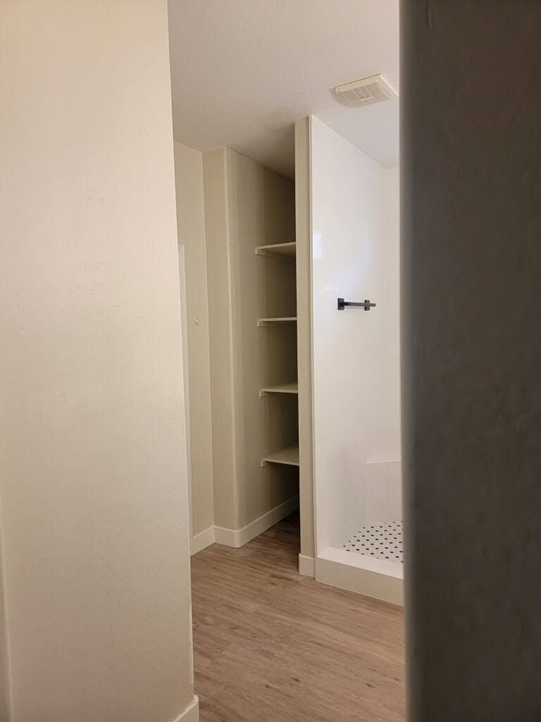 Open closet door in a beige room with empty shelves and wood flooring