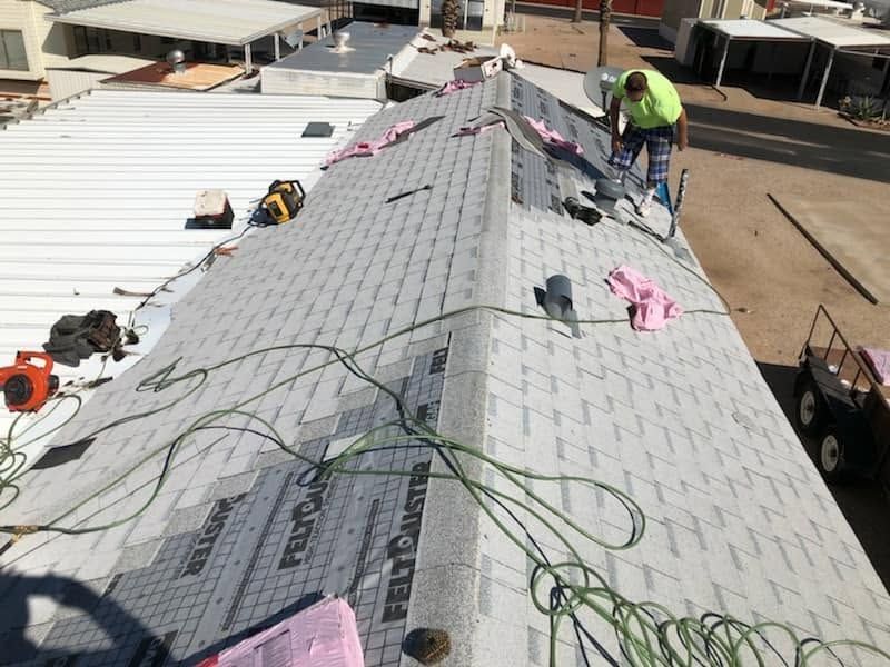 Workers installing roofing on a steep roof, with gray underlayment, tools, and green safety lines.