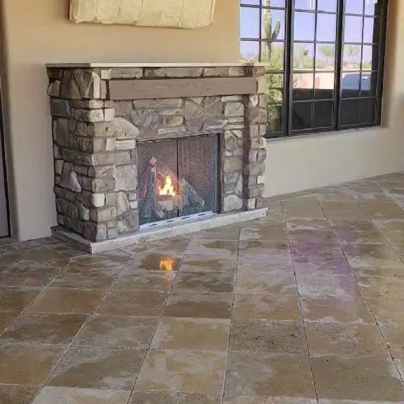Stone fireplace with a small fire in a tiled living room beside a large window.