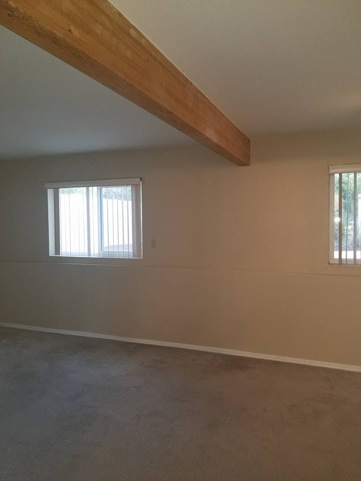 Empty beige living room with carpet, exposed wooden beam, and two small windows