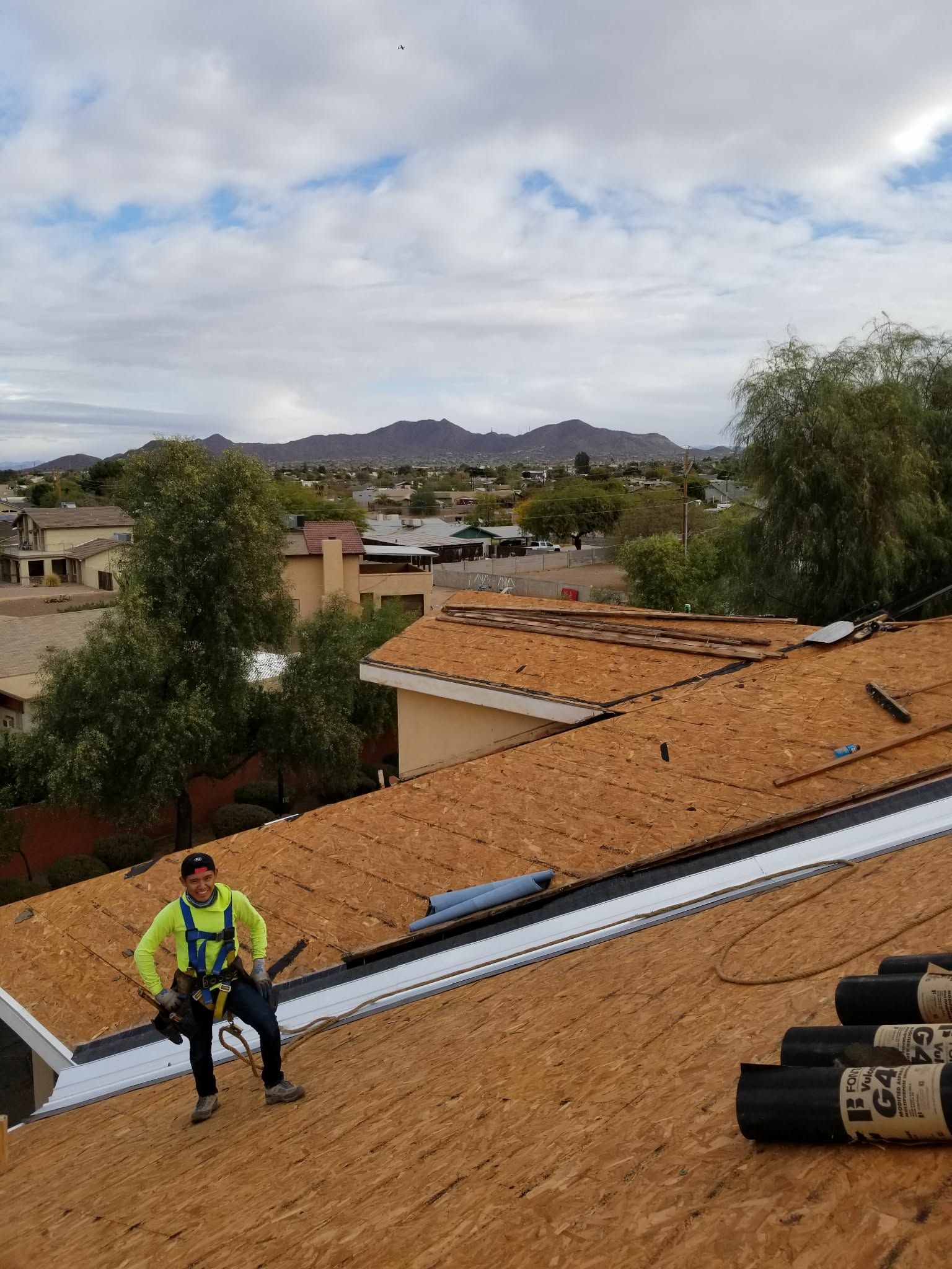 Worker on a rooftop with orange tiles, inspecting solar panels under a cloudy sky.