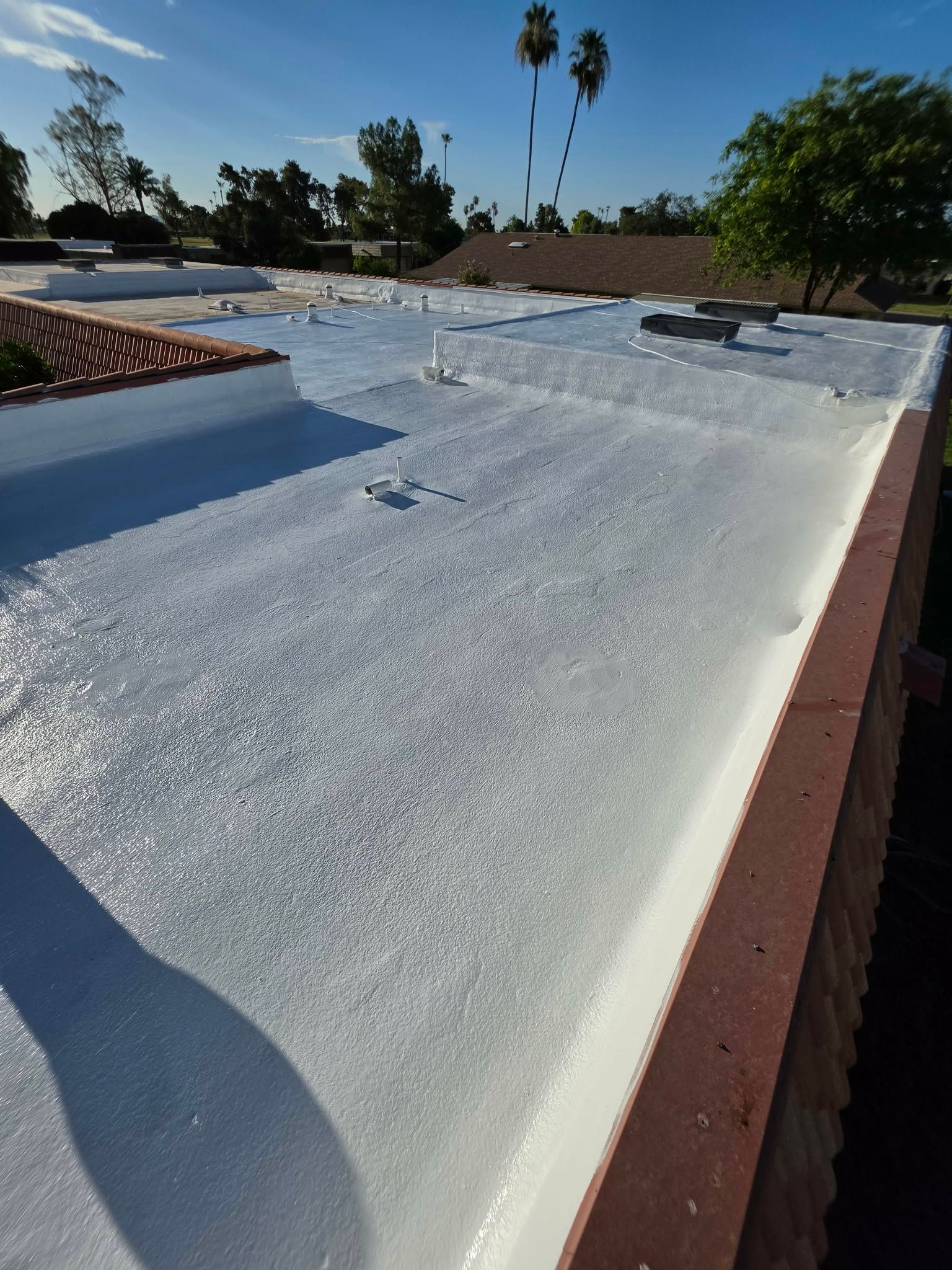 White flat rooftop with vents and skylights under a clear blue sky