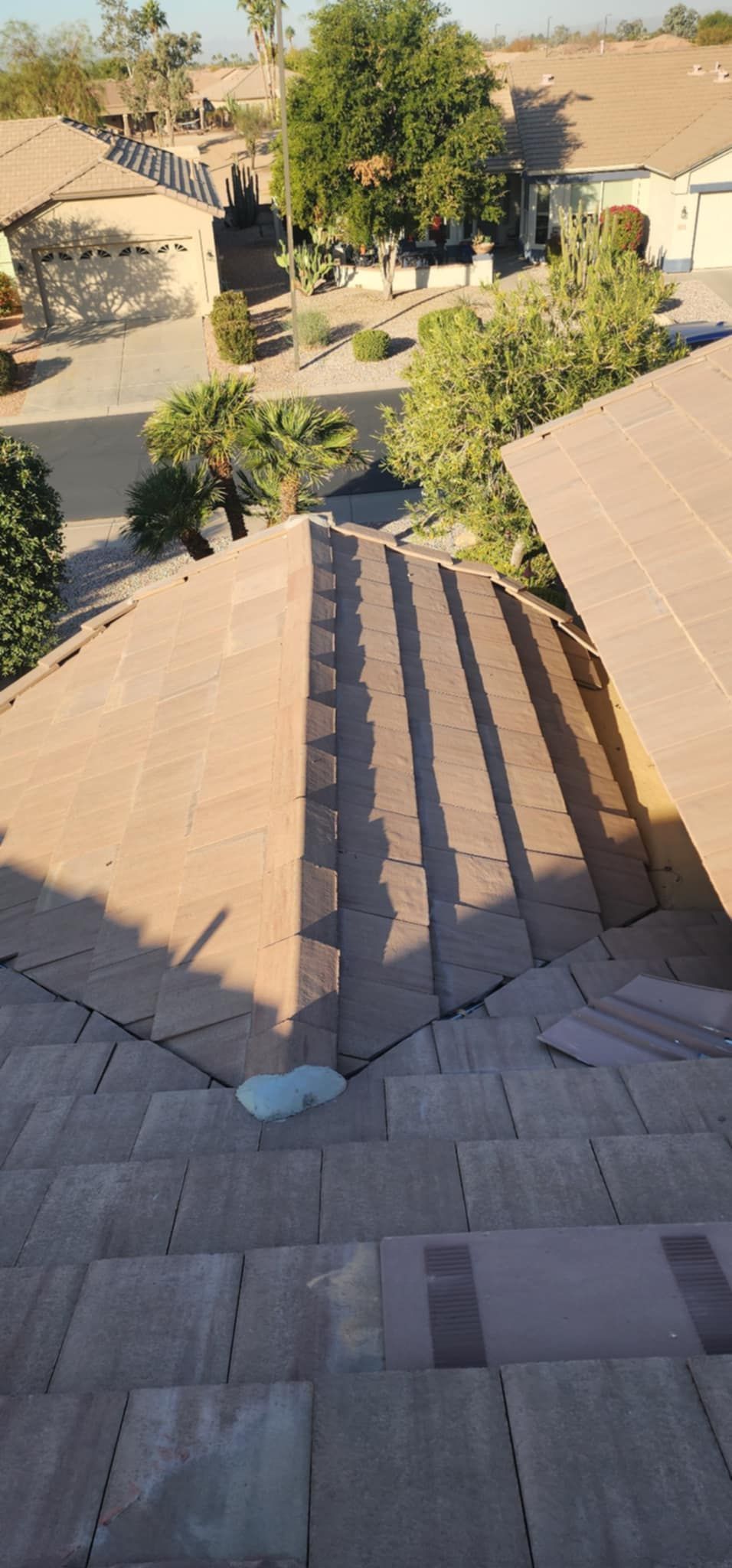 Steep tiled roof with solar panels overlooking trees and tan houses in a desert neighborhood