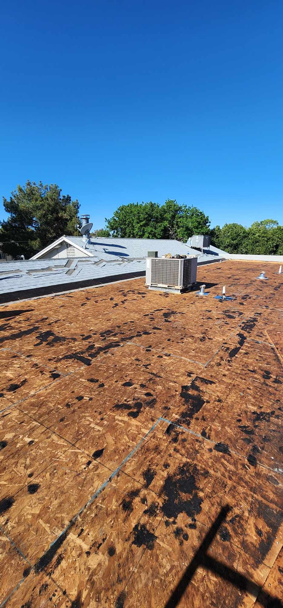 Rooftop under construction with brown roofing material, vents, and blue sky overhead