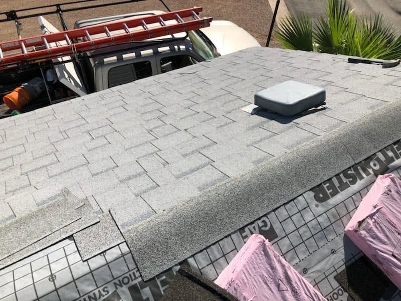 Gray shingle roof with a rooftop vent, seen beside a ladder and covered items below.