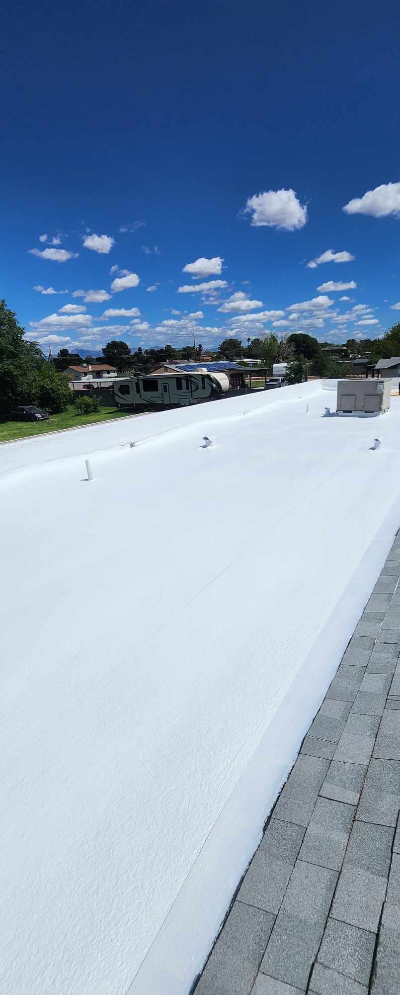 Rooftop with a bright blue sky and clouds above a white surface and gray pavers.