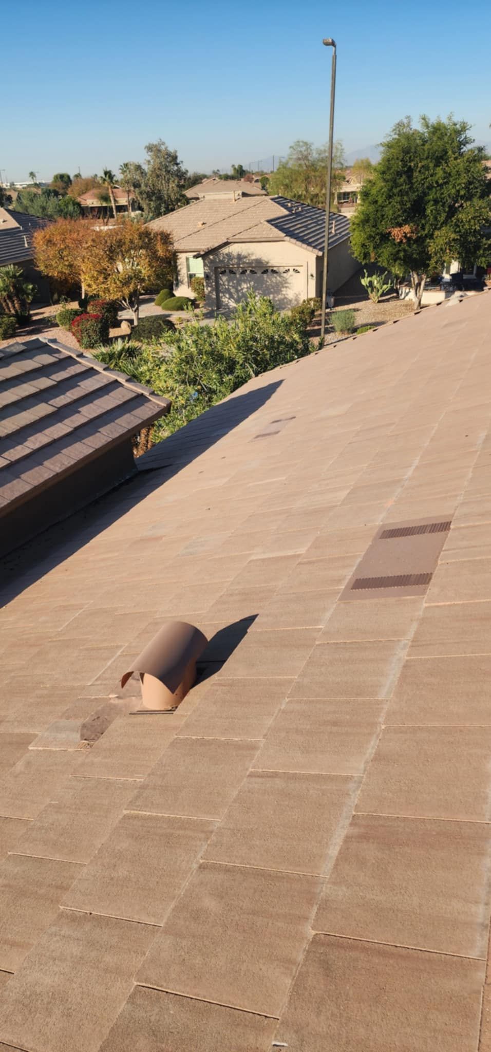 Rooftop shingles with a vent pipe, overlooking trees and houses in a sunny neighborhood