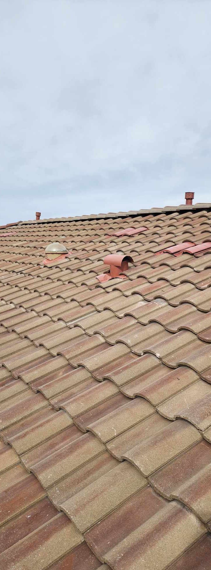 Red tiled roof with a small rooftop vent under a cloudy sky