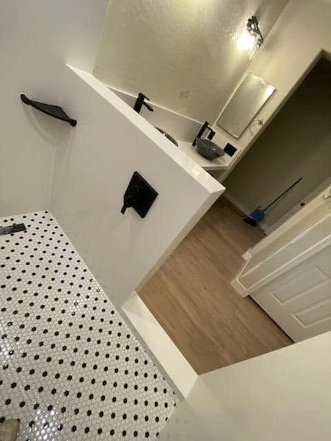 Bathroom with black-and-white dotted shower curtain, white partition, sink, and open door to hallway.