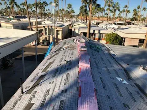 Roof under construction with pink insulation, surrounded by palm trees and desert buildings