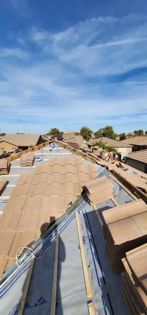 Rooftop view of tan shingle roofs under a blue sky, with a construction worker on the ridge.