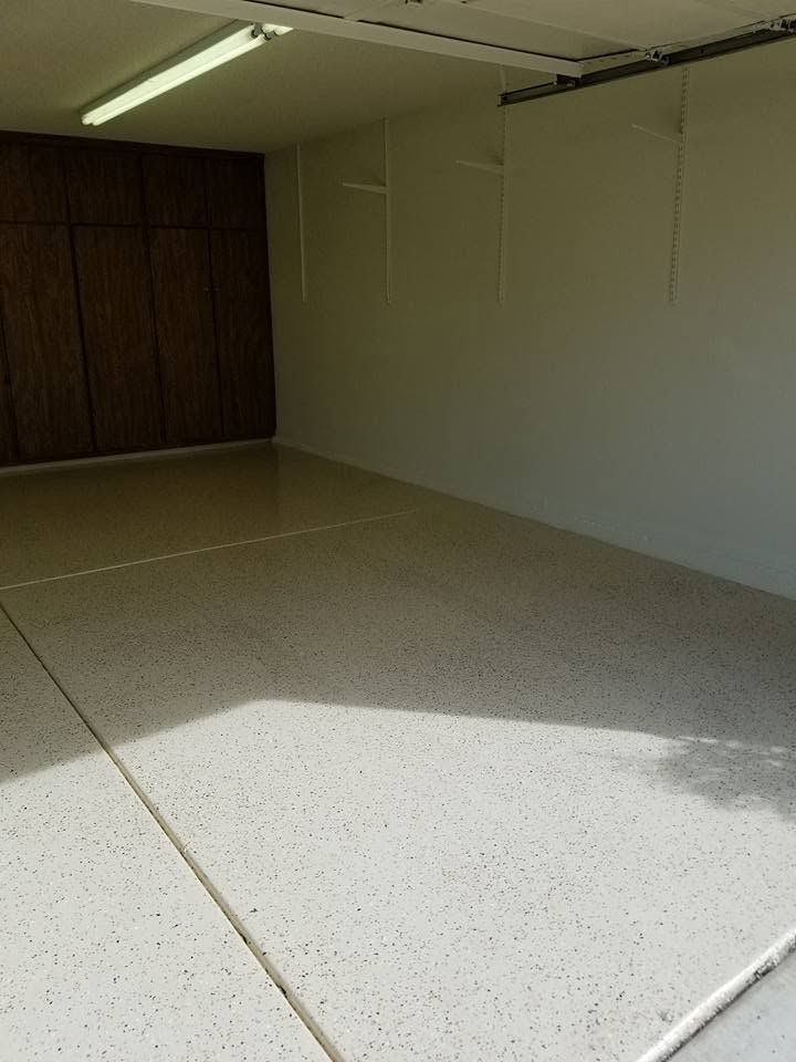 Empty indoor room with white walls, speckled floor, fluorescent lights, and dark cabinets at the back.