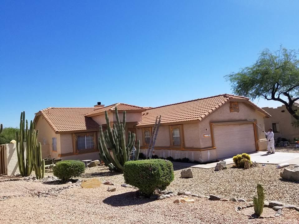 Desert-style stucco house with terracotta roof, garage, cacti, and gravel landscaping under a blue sky